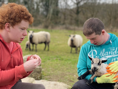 Two boys in a field with lambs at Elidyr Communities Trust.