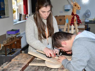Learner with assistant using a hammer to tap in a nail 